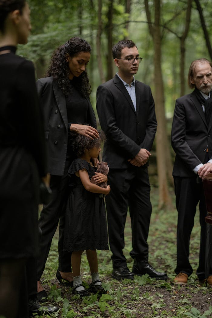 A group of mourners stand solemnly in a forest during a funeral.